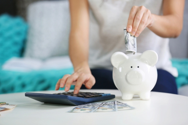 one hand putting money on piggy bank and another hand computing on a calculator depicting minimizing HVAC repair expenses