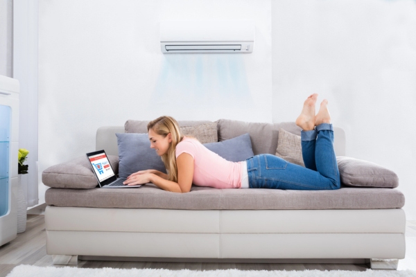 woman keeping cool in front of a ductless air conditioner while working on the couch