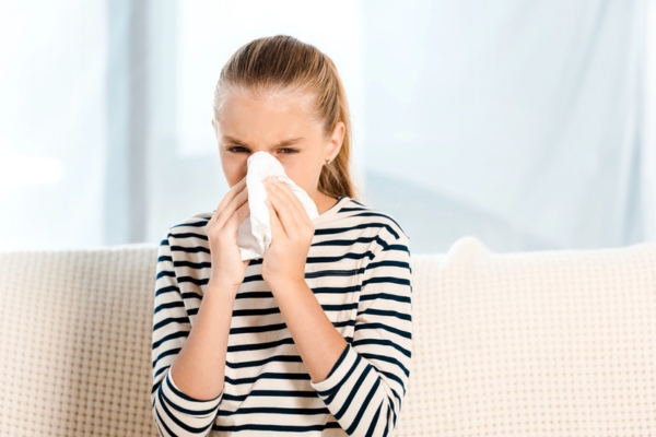 young girl sneezing on a tissue depicting signs you need professional HVAC ductwork cleaning