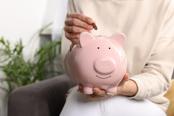 cropped view of a homeowner holding a piggy bank and putting a coin in it depicting fuel savings