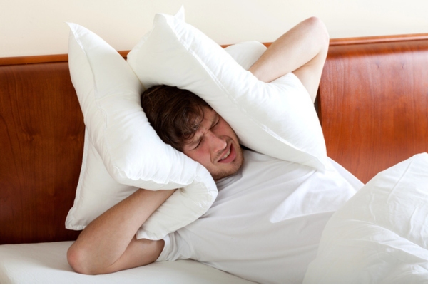 man covering his ears with pillow due to noise from portable AC