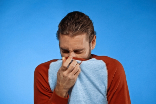 man covering his nose with a shirt due to tap water smelling like sulfur