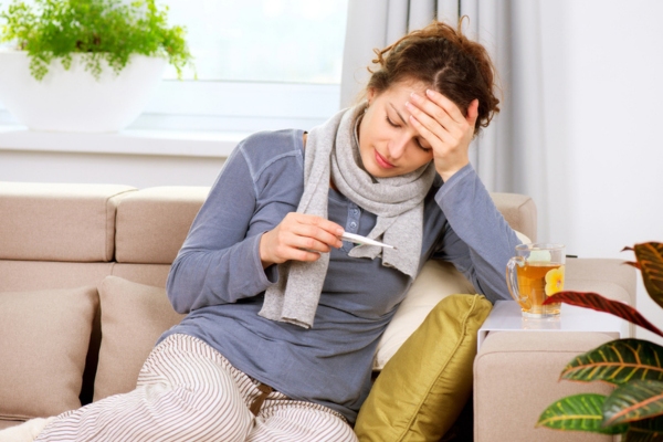 sick woman sitting on the couch holding a thermometer