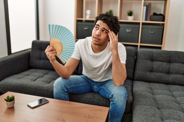 man using hand fan while looking up depicting Preparing for Air Conditioner Emergencies
