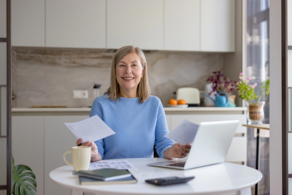 smiling woman computing Energy Savings from an Air Conditioner Upgrade in her kitchen with her laptop and calculator