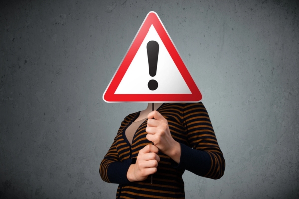 woman holding an exclamation road sign in front of her face depicting Common Air Conditioning Scams