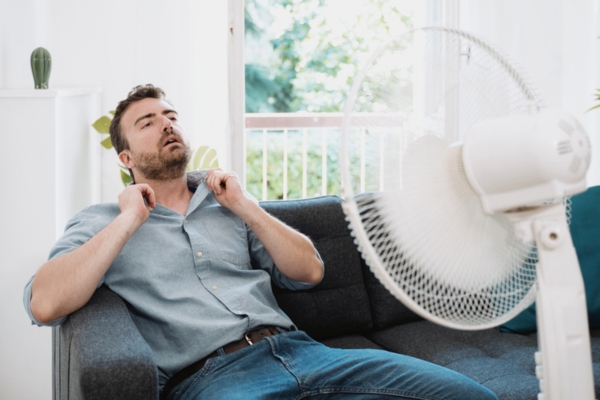 man feeling hot indoors using stand fan due to AC blowing weak air