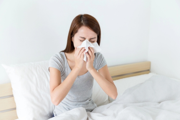 woman sneezing on a tissue in the bedroom depicting indoor air quality
